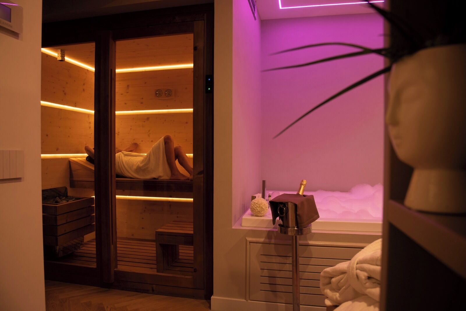 Um quarto de spa com chão de madeira, uma mesa de massagem, uma cadeira de massagem e uma garrafa de champanhe.