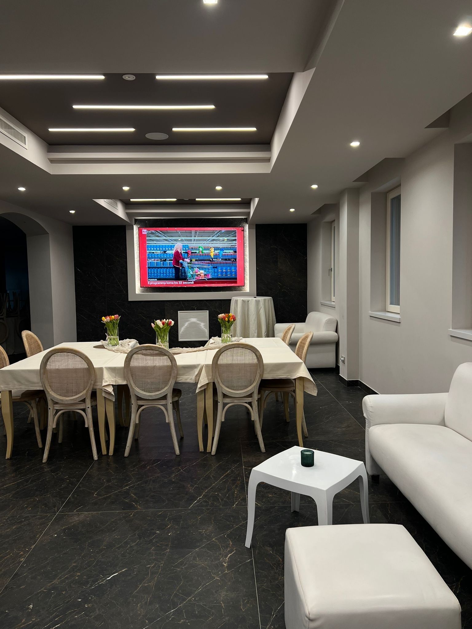 A modern living room with a dining area, a flat-screen TV, and a white sofa.