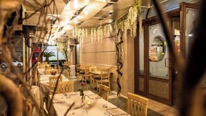 A restaurant with tables set for dining, a large window with a view, and hanging greenery.