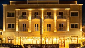 A multi-story hotel with balconies, a central entrance, and a parking area.