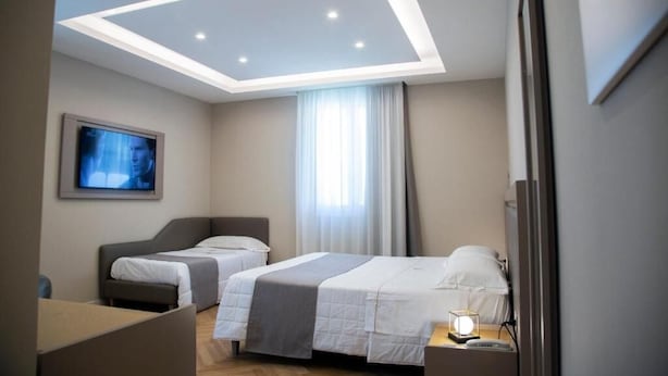 A hotel room with two beds, a ceiling light, a TV, and a bedside table with a lamp.