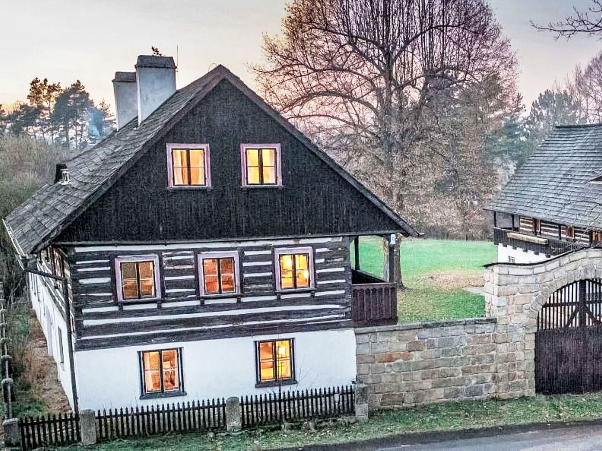A traditional log cabin with a stone foundation, multiple windows, and a stone gate.