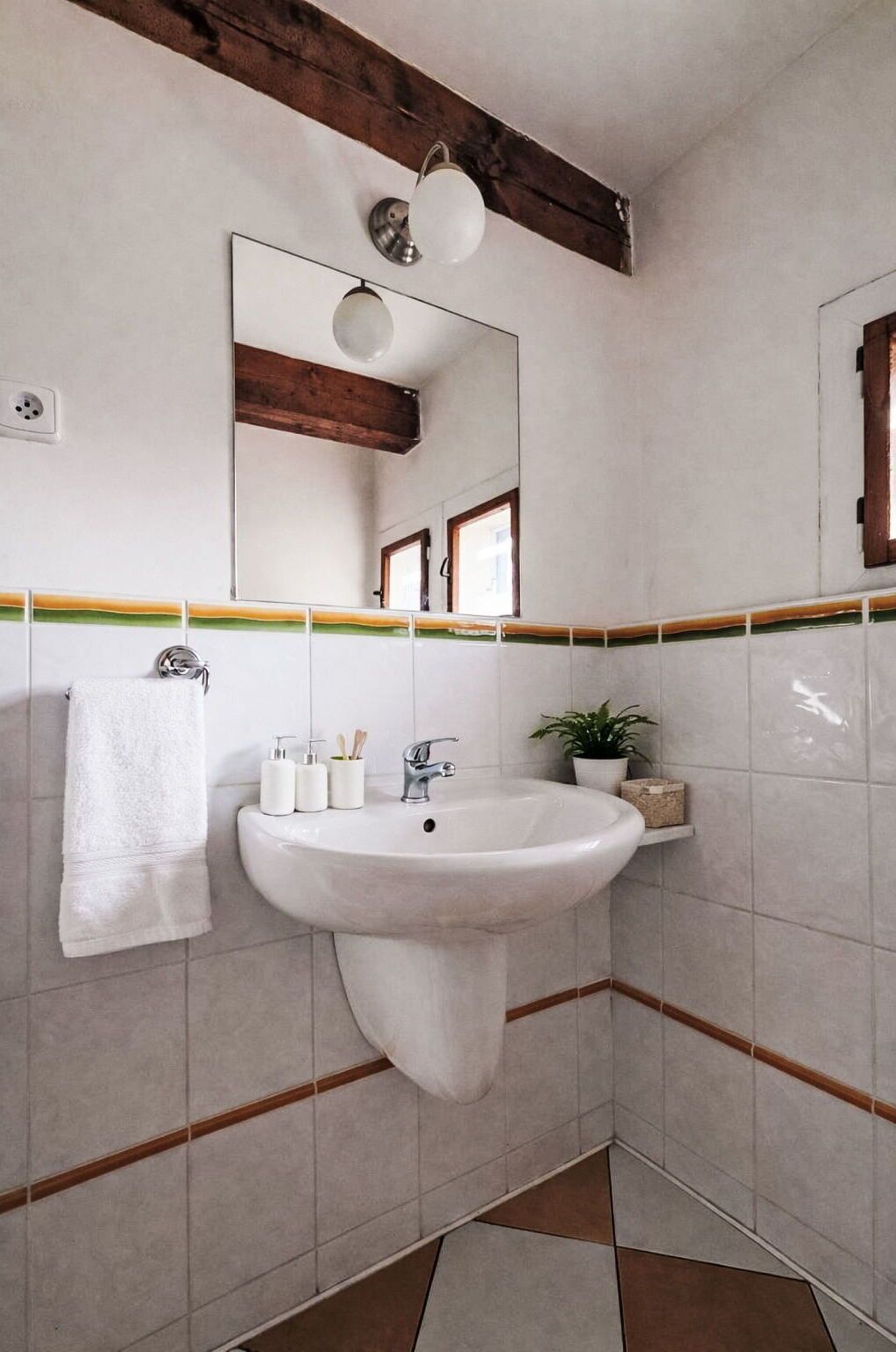 Une salle de bain avec un lavabo blanc, une serviette, un miroir et une plante en pot.