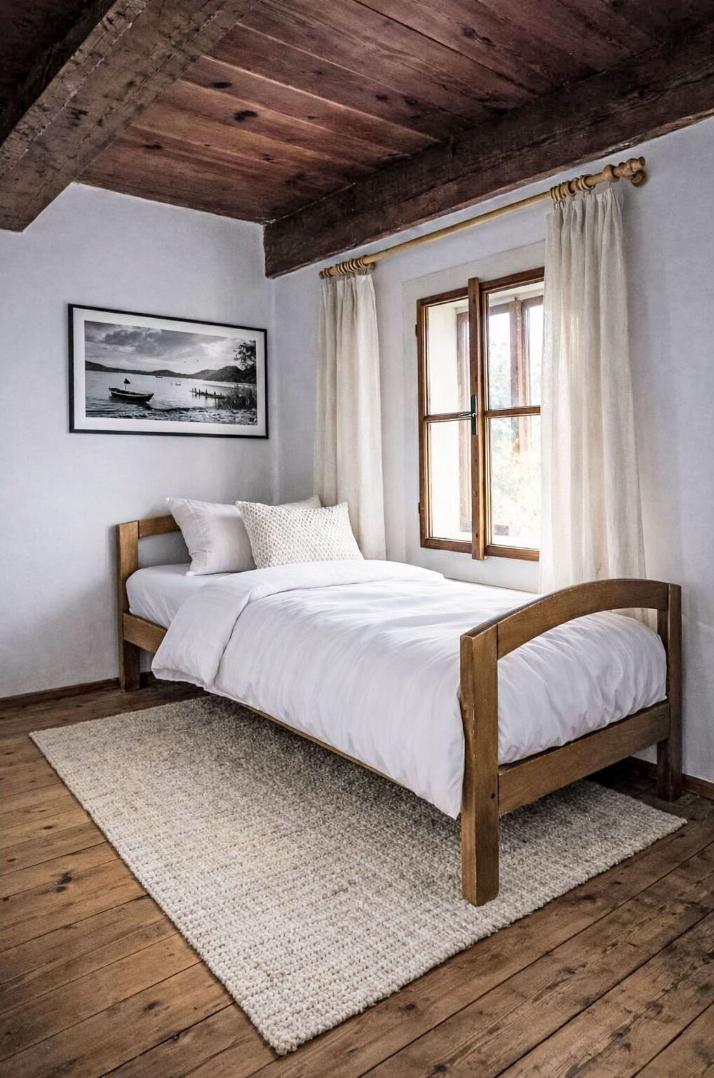 Ein Bett mit Holzrahmen, weißer Bettwäsche und einem Teppich auf Holzdielen.