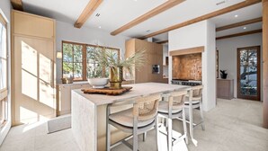 Une cuisine moderne dotée d’un îlot central, de poutres en bois et de grandes fenêtres.