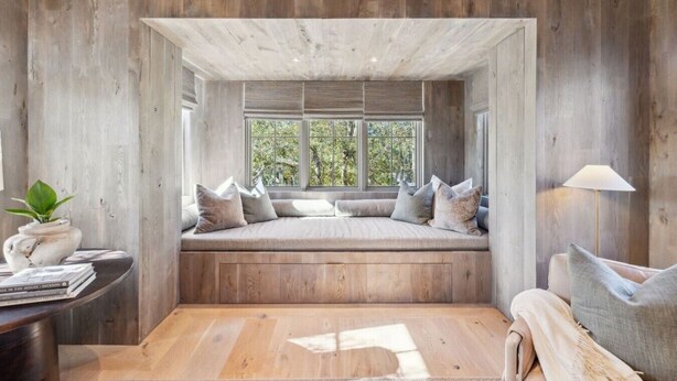 Une pièce dotée d’une banquette intégrée avec des coussins, d’un plancher en bois et d’une fenêtre donnant sur un paysage verdoyant.