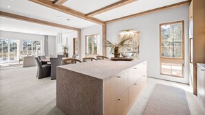 Une cuisine spacieuse dotée d’un îlot central, de grandes fenêtres et d’un coin repas aménagé avec du mobilier moderne.