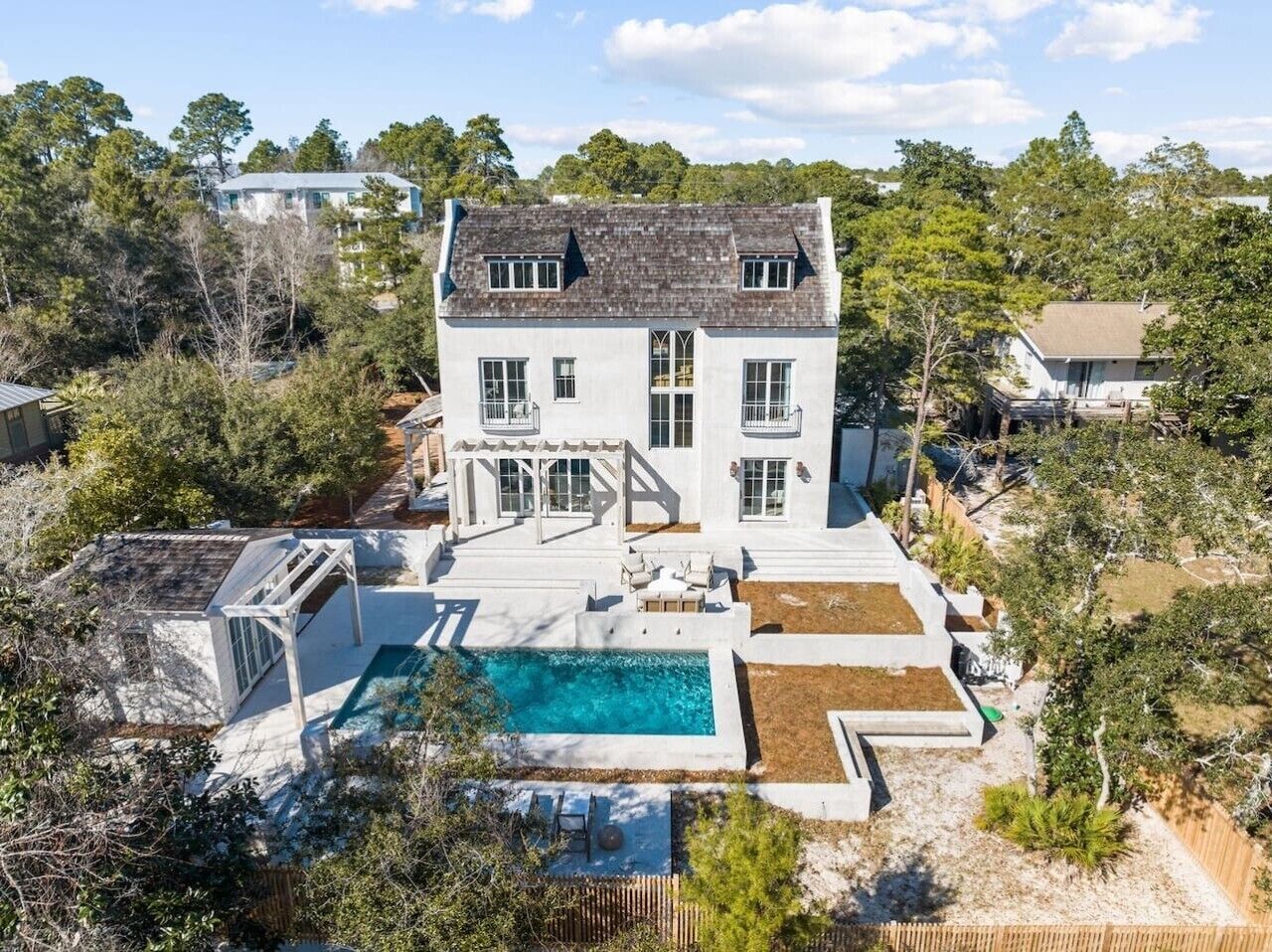 A two-story house with a swimming pool, surrounded by trees and a fenced yard.