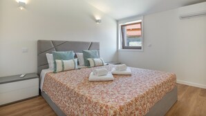 Una camera da letto con un letto, cuscini, un comodino, una finestra e un condizionatore d'aria.