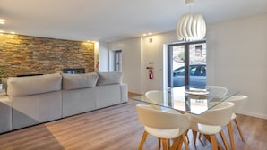 Un'area soggiorno moderna con parete in pietra, un divano, un tavolo da pranzo in vetro e sedie, e una lampada a soffitto.