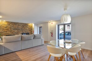 Un espace de vie moderne avec un mur en pierre, un canapé, une table à manger en verre avec des chaises et un luminaire suspendu au plafond.