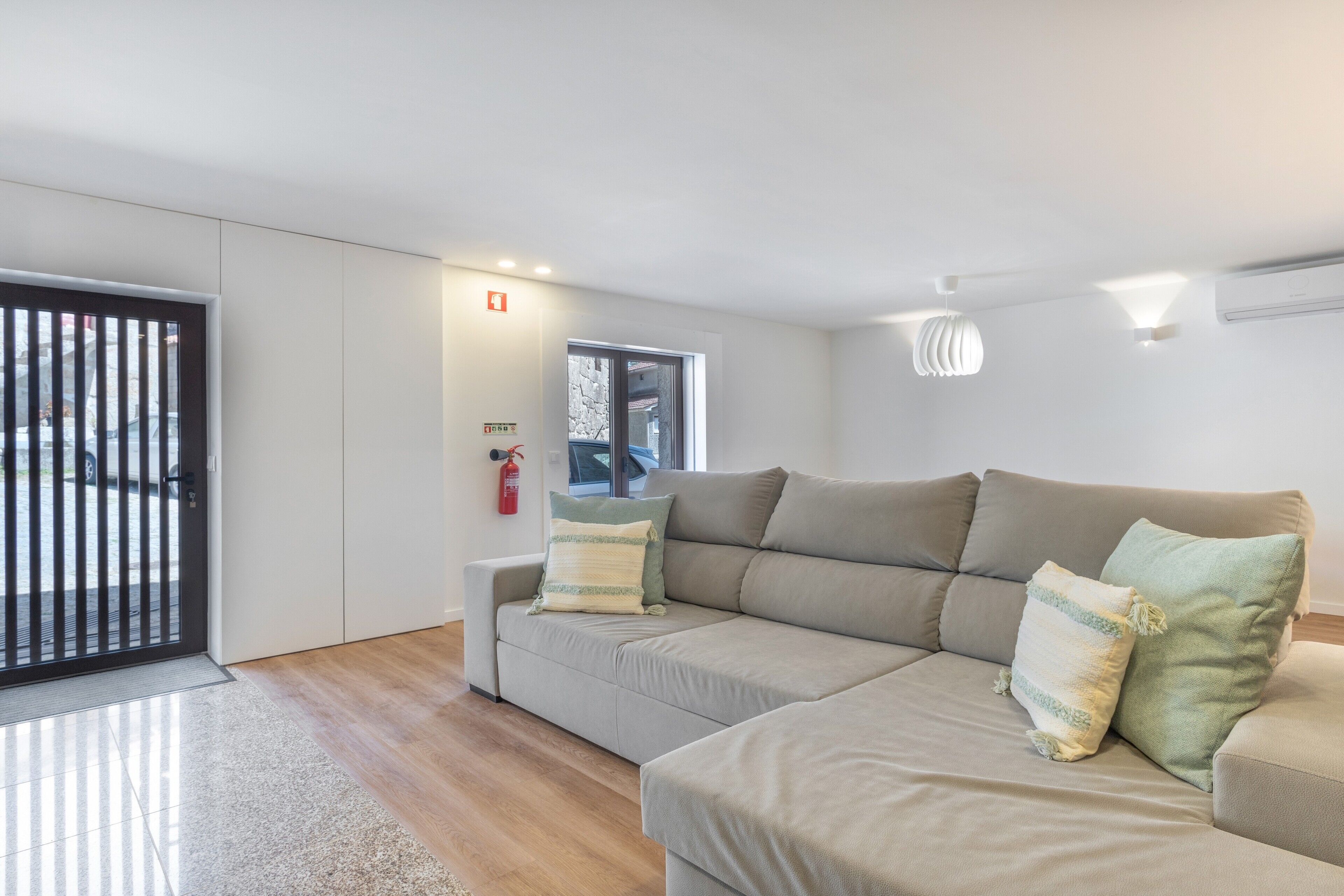 A modern living room with a sofa, a fire extinguisher, and a window.