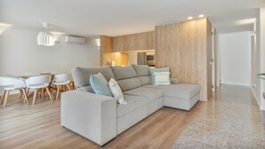 Un soggiorno moderno con un divano componibile, una zona pranzo con un tavolo in vetro e una cucina sullo sfondo.