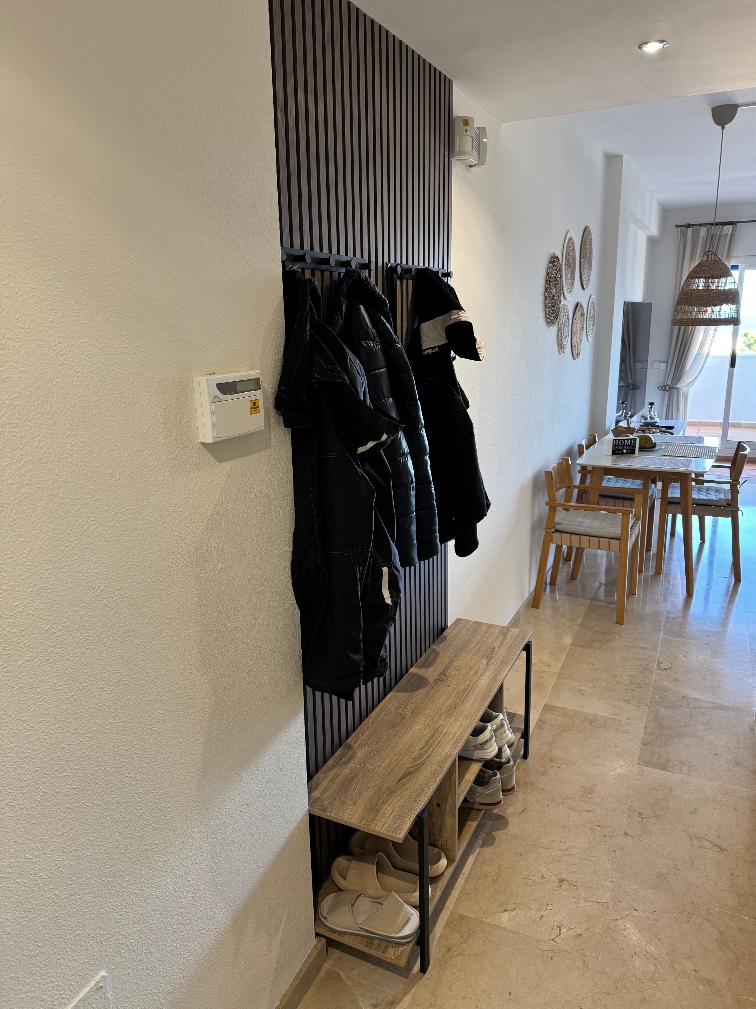 A hallway with a coat rack, a bench, and a dining area with a table and chairs.