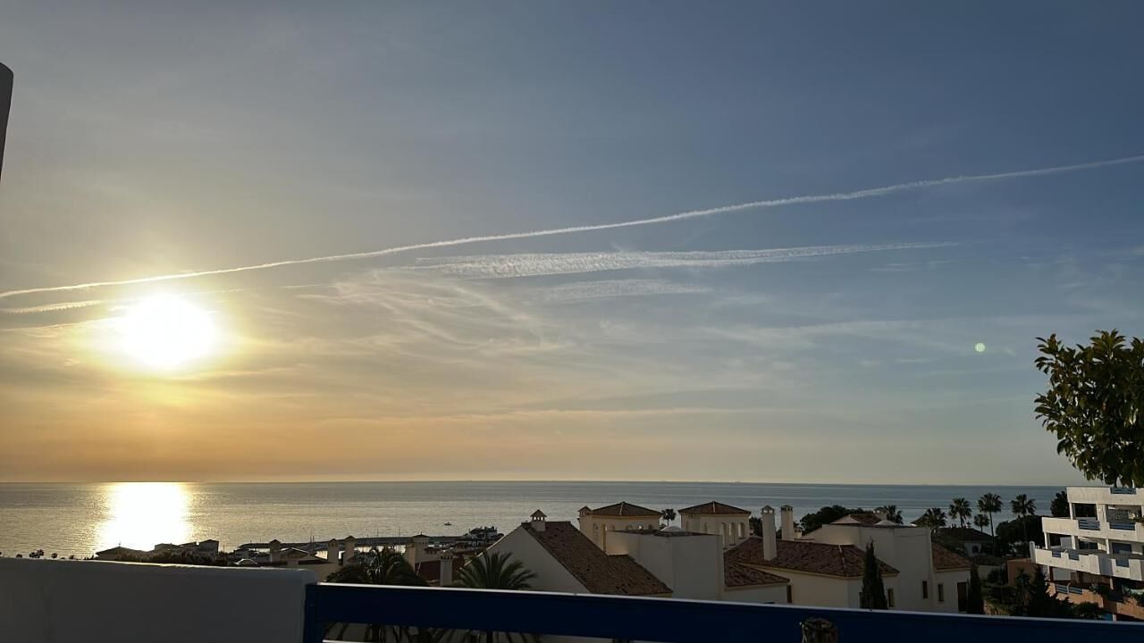 Vista costera con cielo despejado, un sol poniente y edificios en primer plano.