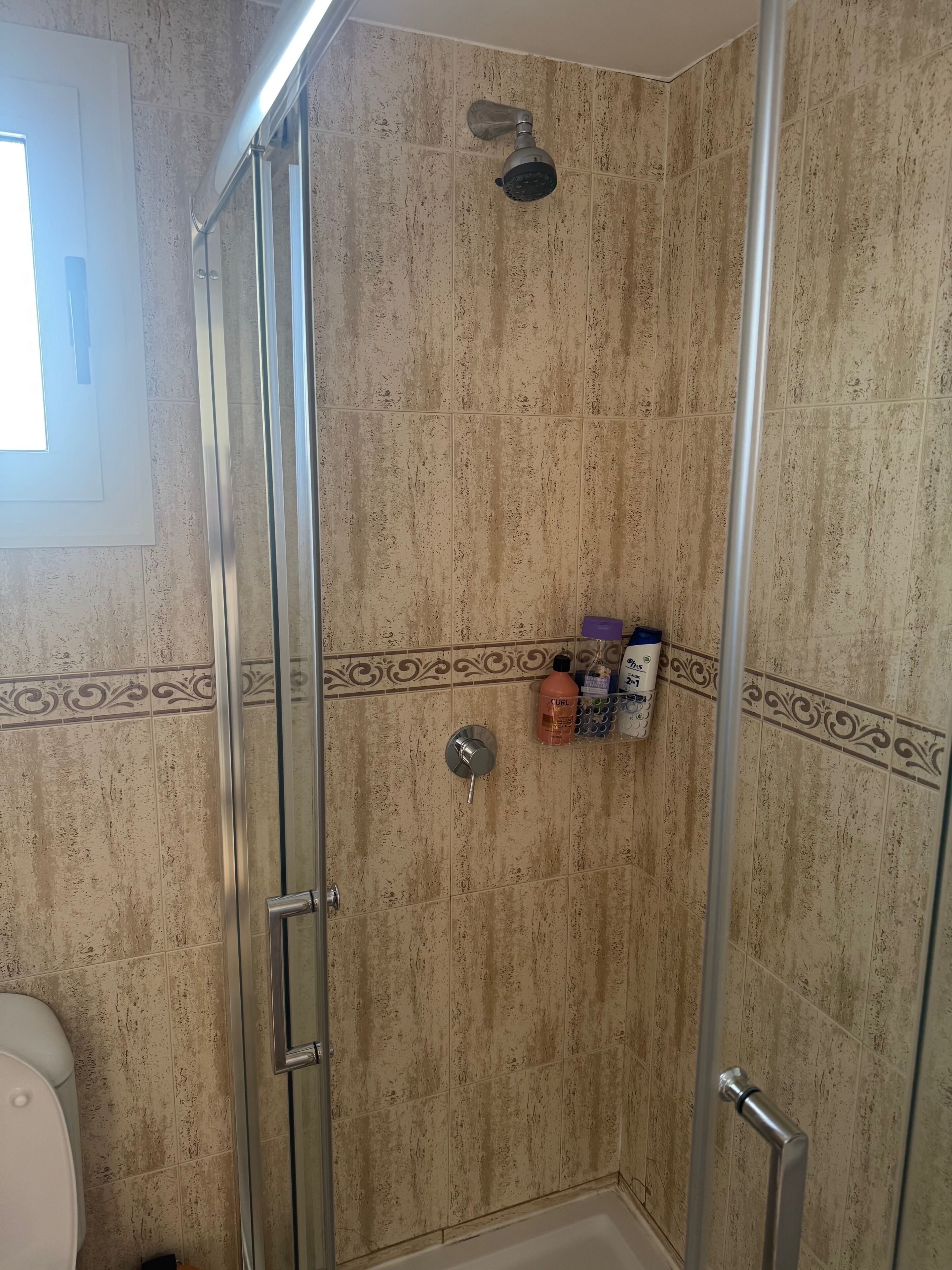 Un espace douche doté d’une porte en verre, d’un pommeau de douche et d’un mur carrelé.