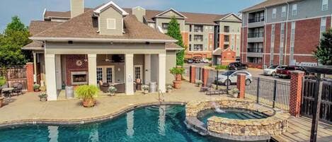 A pool area with a stone water feature, a covered seating area, and a brick building in the background.