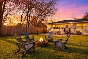 Un jardin avec un foyer et des fauteuils Adirondack, une clôture en bois et une maison dotée d’une terrasse.