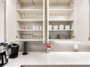A kitchen with white cabinets, a coffee maker, and a spice rack. - Walk to OU - Spacious 4BR with Fire Pit (Norman)