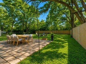 A patio with a table and chairs, surrounded by a wooden fence and lush green grass. - Walk to OU - Spacious 4BR with Fire Pit (Norman)