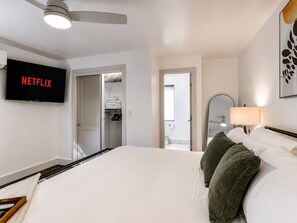 Une chambre d’hôtel avec un lit, un téléviseur fixé au mur, une armoire et une salle de bain visible à travers une porte ouverte.