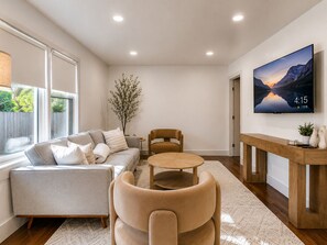A modern living room with a sofa, armchairs, a coffee table, and a TV mounted on the wall. - Walk to OU - Spacious 4BR with Fire Pit (Norman)