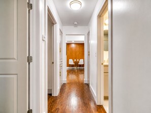 Un couloir avec des portes blanches, un plancher en bois et un coin repas comprenant des chaises et une table.