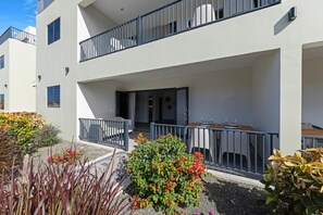 Ein modernes Mehrfamilienhaus mit Balkonen, einer überdachten Außenlounge und einem Garten mit verschiedenen Pflanzen.