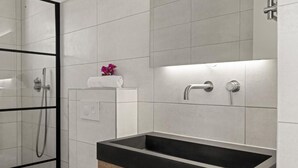 A modern bathroom with a rectangular sink, a glass shower enclosure, and a towel rack with a rolled towel. - Apartement Luna Mambo Beach (Willemstad)