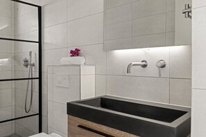 Ein modernes Badezimmer mit einem rechteckigen Waschbecken, einer Duschkabine aus Glas und einem Handtuchhalter mit einem aufgerollten Handtuch.