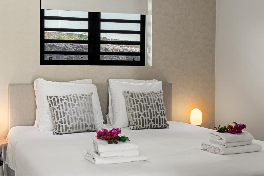 Un dormitorio con cama, almohadas, una ventana y una lámpara fijada a la pared.