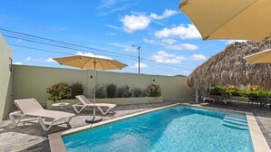 A swimming pool with lounge chairs and umbrellas, surrounded by a low wall and potted plants. - Apartement Luna Mambo Beach (Willemstad)