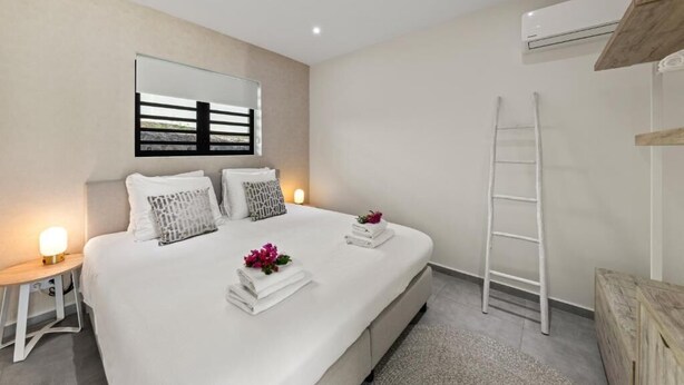 A modern bedroom with a bed, bedside tables, a ladder, and an air conditioning unit. - Apartement Luna Mambo Beach (Willemstad)