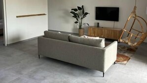A modern living room with a sofa, a hanging chair, a flat-screen TV, and a potted plant. - Apartement Luna Mambo Beach (Willemstad)