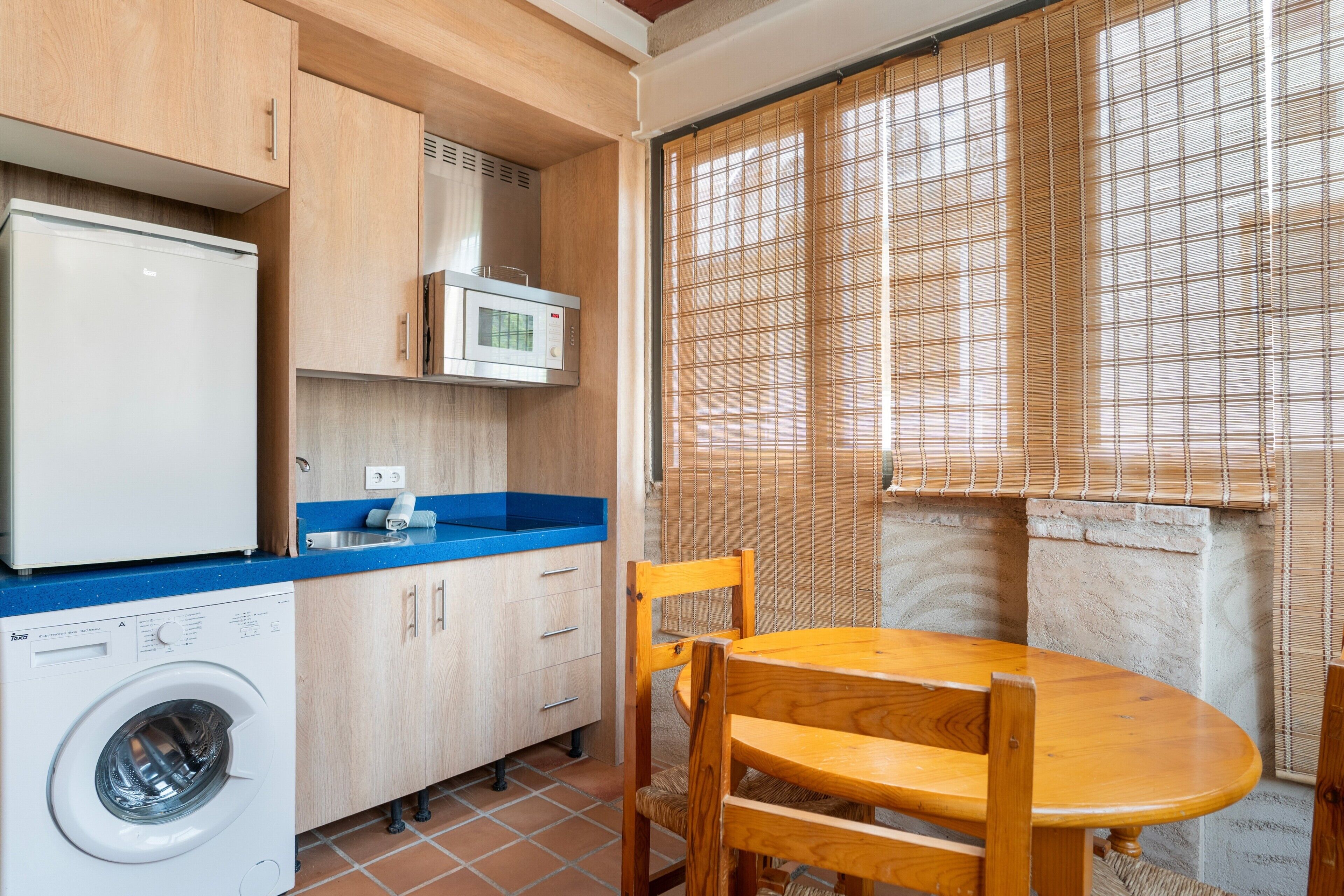 Cocina compacta con lavadora, microondas y comedor con mesa y sillas.