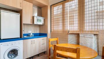 Cocina compacta con lavadora, microondas y comedor con mesa y sillas.