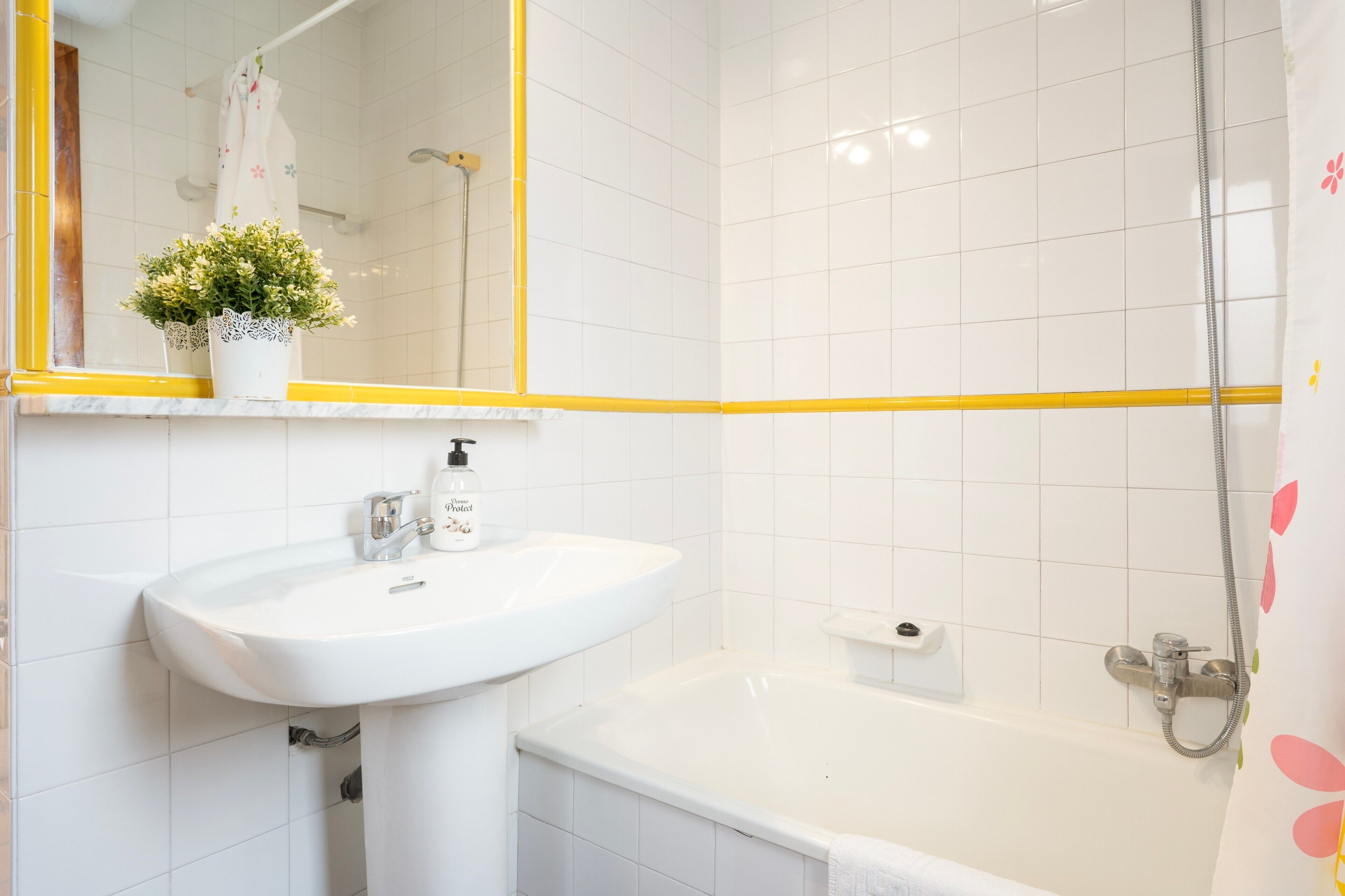 A bathroom with a white sink, a mirror with a yellow frame, a shower, and a potted plant.