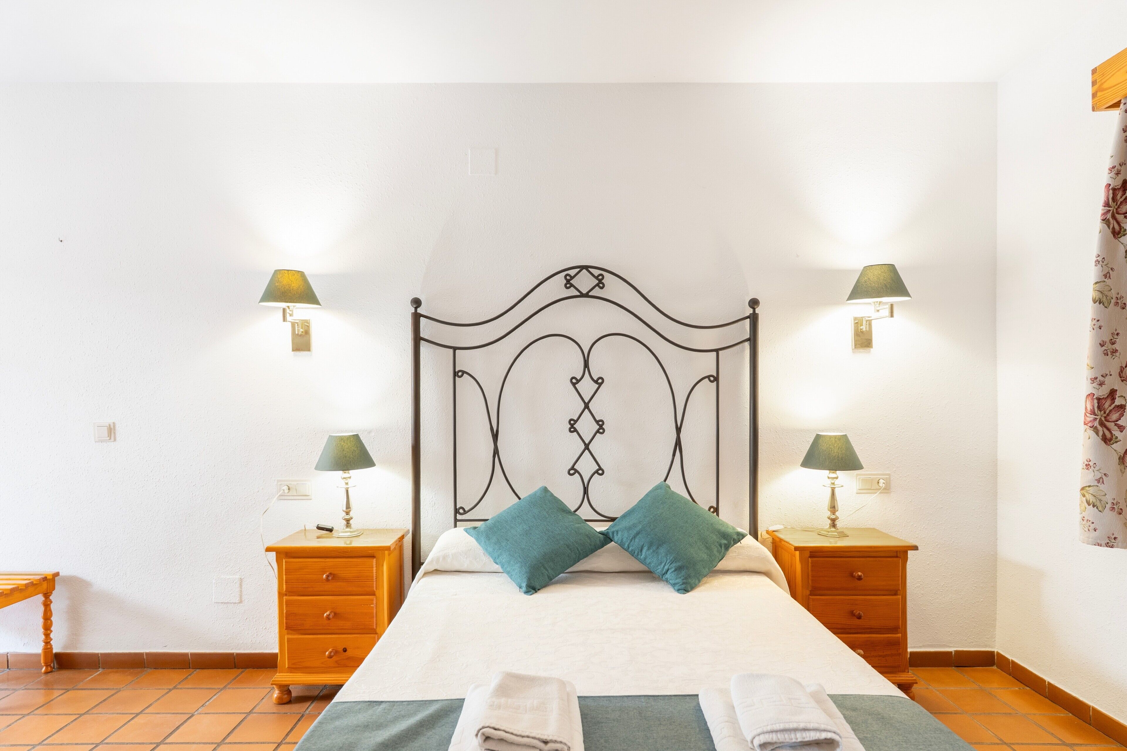 A bed with a headboard, two bedside tables, two lamps, and two pillows.