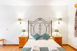 A bed with a headboard, two bedside tables, two lamps, and two pillows.