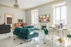 A spacious living room with a large sofa, a dining table set for four, and a fireplace. - Sant'Angelo Deluxe Apartment (Roma)