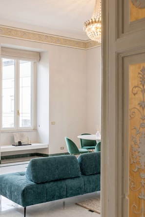 A room with a large window, a green sofa, a chandelier, and a small table with candles. - Sant'Angelo Deluxe Apartment (Roma)