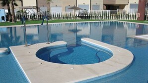 A swimming pool with a circular hot tub in the center, surrounded by a tiled deck. - Varudi1.09 (Torrevieja)