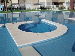 Ein Schwimmbecken mit einem runden Whirlpool in der Mitte, umgeben von einer gefliesten Terrasse.