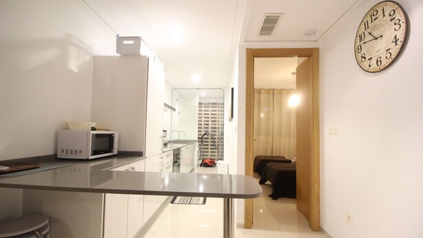 A modern kitchen with a microwave, a glass-top table, and a view into a bedroom. - Varudi1.09 (Torrevieja)