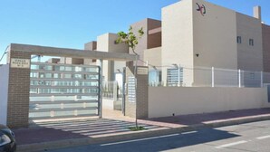 A modern building with a gated entrance, a clear sky, and a tree in front. - Varudi1.09 (Torrevieja)