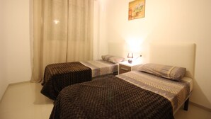 A room with two beds, a nightstand, a lamp, and a painting on the wall. - Varudi1.09 (Torrevieja)