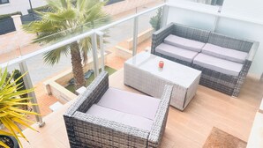 A balcony with wicker furniture, including a sofa and a table, and a palm tree. - Duplez Zenia Beach (Orihuela)
