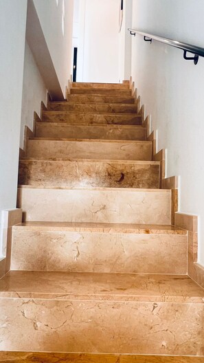 A staircase with a handrail, made of a light-colored stone or marble, leading to an upper floor.