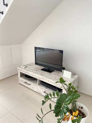 A modern living room with a flat-screen TV on a rustic wooden TV stand, a potted plant, and a white wall.