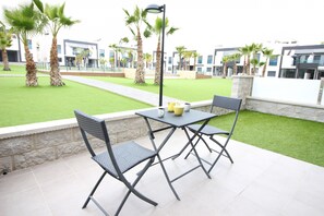 Un patio exterior con mesa y sillas, rodeado de palmeras y un césped bien cuidado.